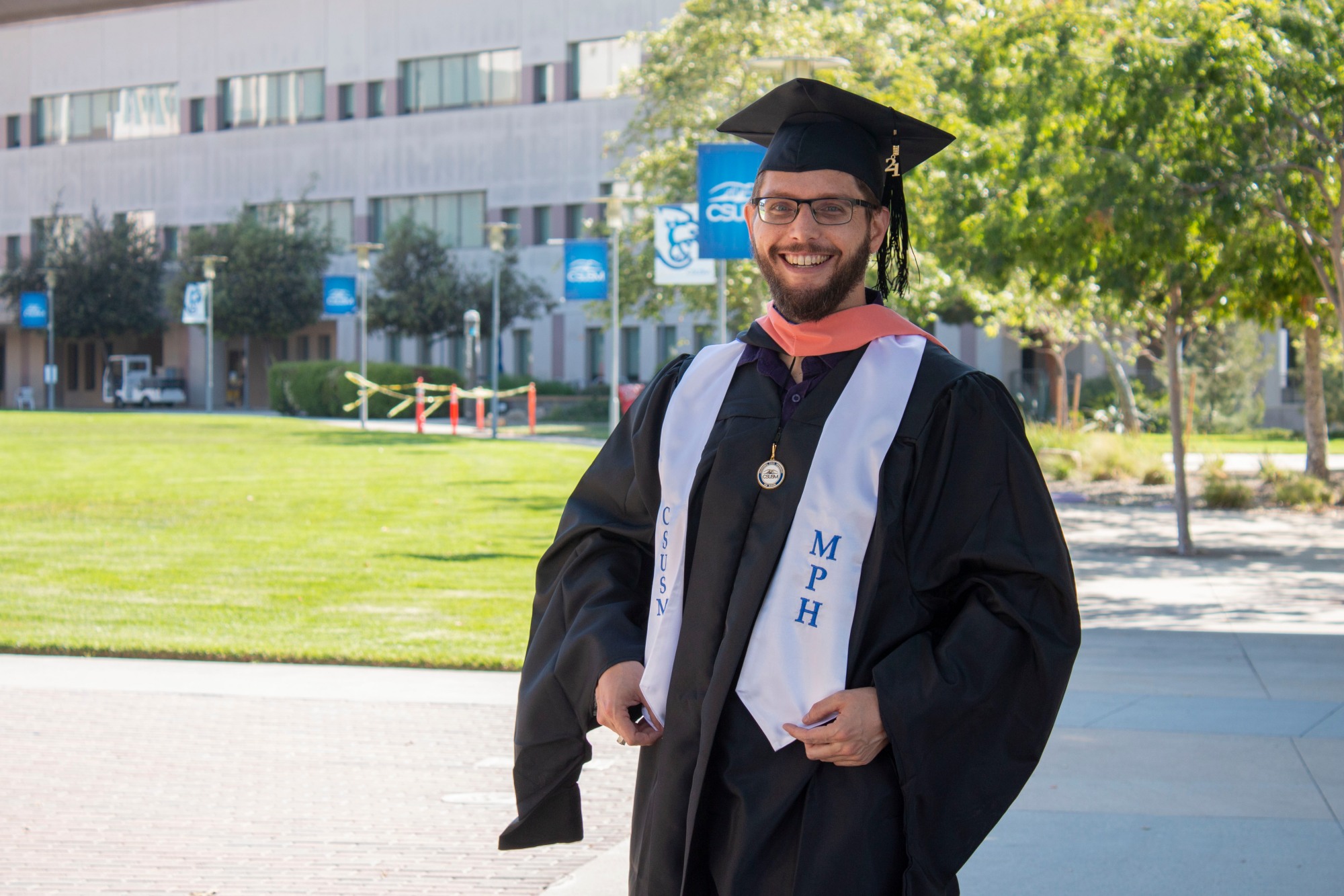 Rick J Nash in his graduation cap and gown on campus at CSUSM also wearing his MPH stole and hood.